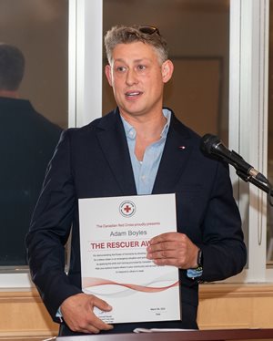 Adam Boyles standing in front of a podium, with the rescuer award in hand.