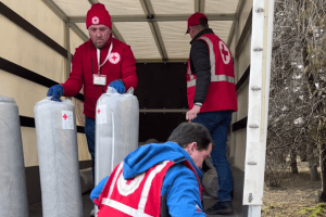 Three individuals unload mattresses from a truck.