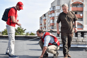 Three individuals inspect the roof of a building.