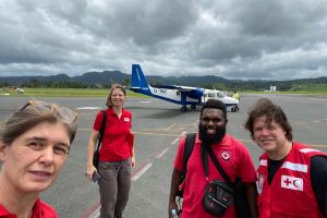 Red Cross personnel smile in front of a helicopter