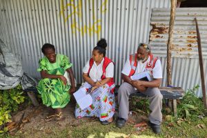 Two Red Cross personnel sit outside while speaking with a woman