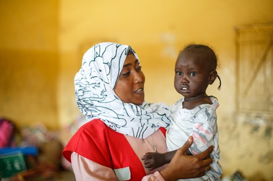 Sudan Red Crescent Society volunteer nurse Wajdan Hassan Ahmed holds a young child