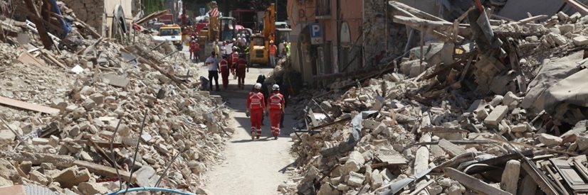 Rubble from demolished buildings and rescue workers walking along the road.